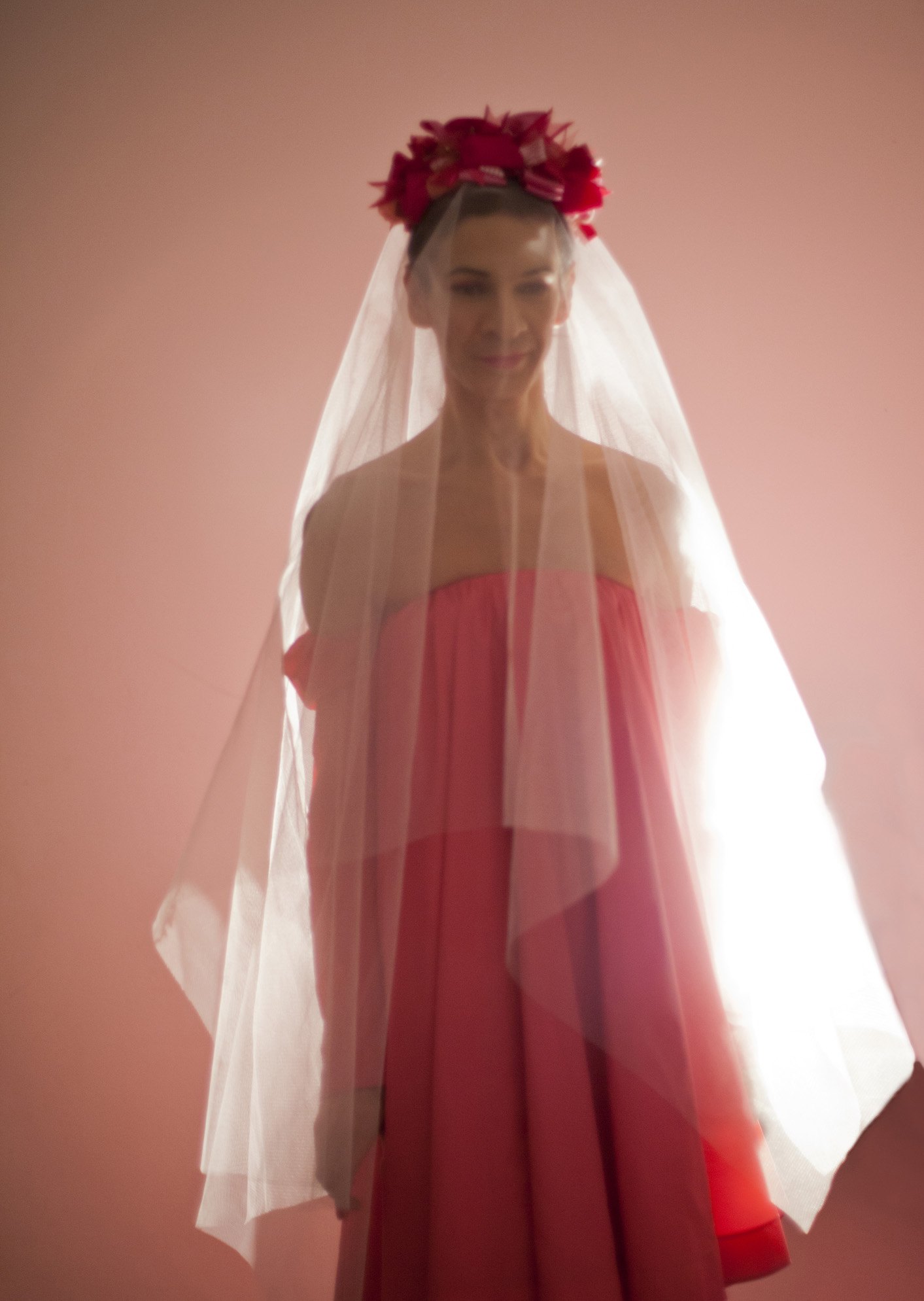 The artist wears a pink dress and veil, with a flower crown.