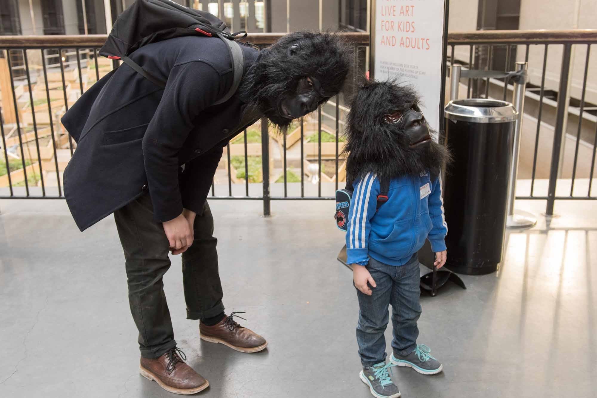 A young person and their parent wear gorilla masks in the Tate Modern Turbine Hall.