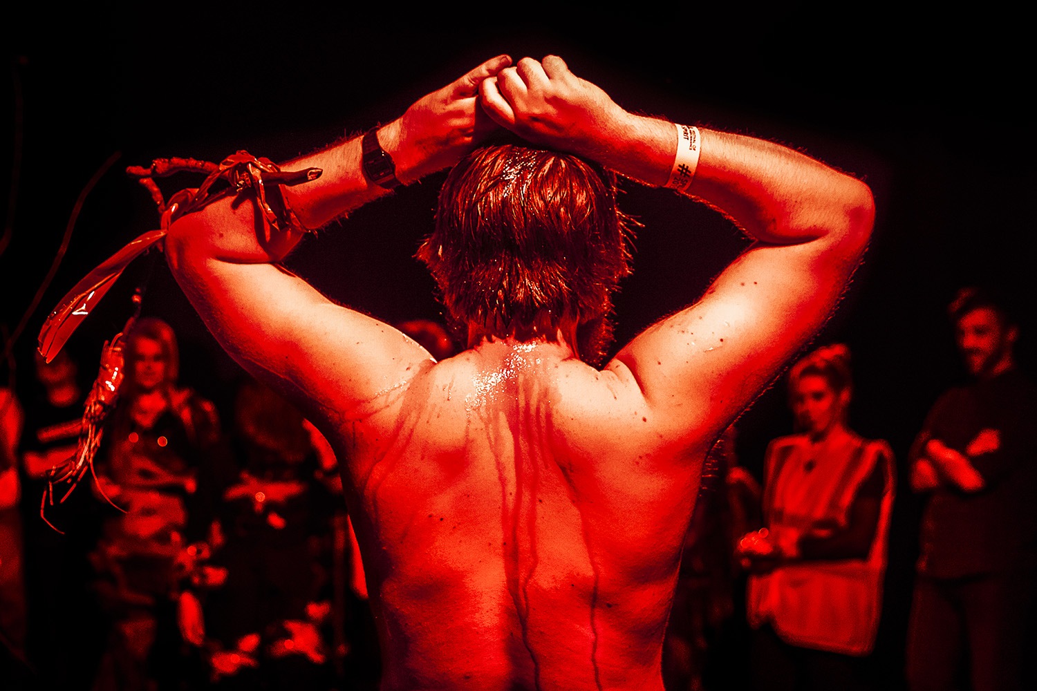 Daniel Oliver's back with arms raised from Weird Seance Incredible Interquel Spectactle, in red tint