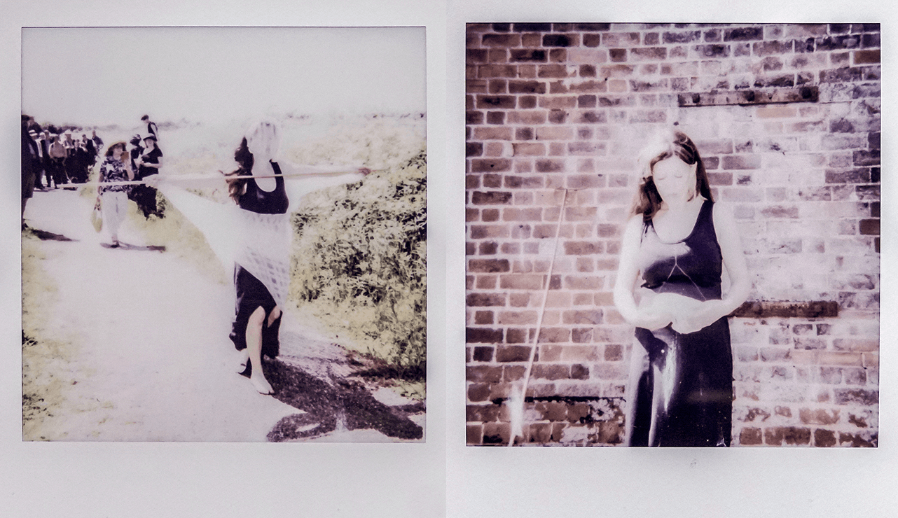 Poppy Jackson is walking along a path in front on a group of people on a sunny day. She is wearing all black and is bare-foot, whilst holding out a large horizontal wooden stick in front of her. This is taken in a polaroid style