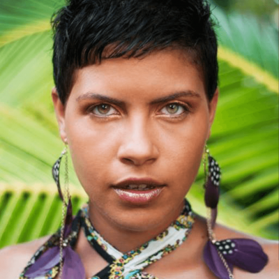 Ria Righteous stood in a tropical garden wearing a colourful floral dress and purple floral earrings