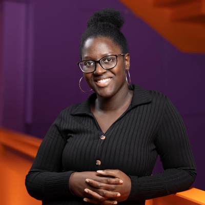 Tania Camara stood smiling, wearing a black shirt, whilst leaning against an orange-lit balcony
